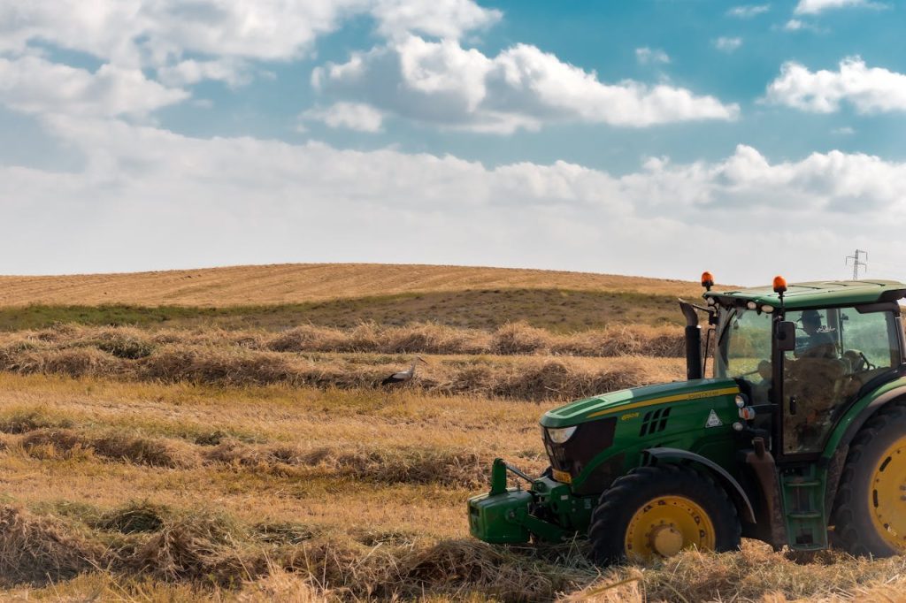 anonymous-farmer-in-tractor-driving-on-grassy-field-7939090 Unrecognizable male farmer driving tractor on dried grassy meadow in countryside near hills under cloudy blue sky in daytime